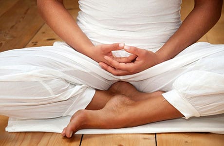 Person in white clothing seated in meditation on a wooden floor