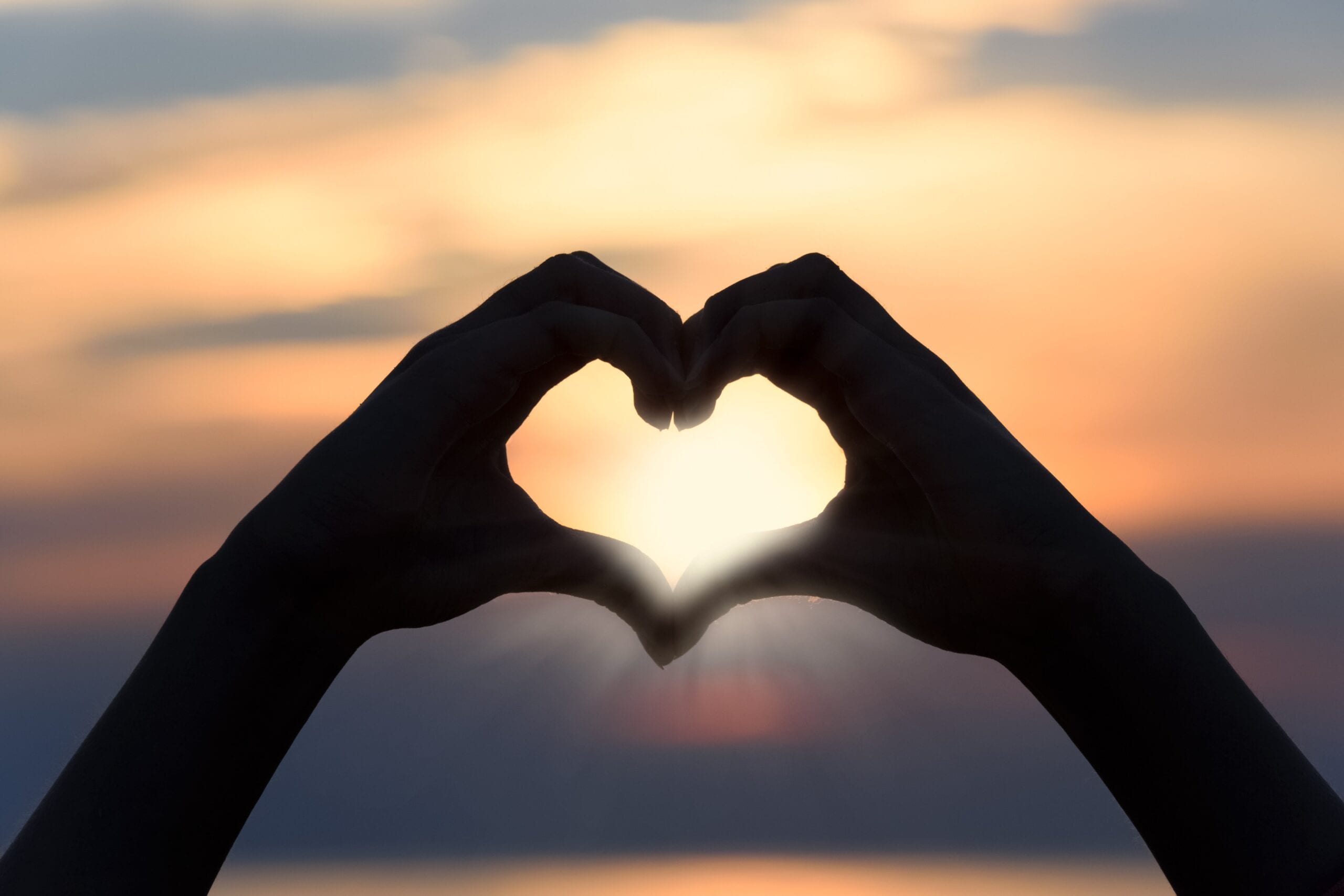 Hands forming a heart shape against a sunset sky