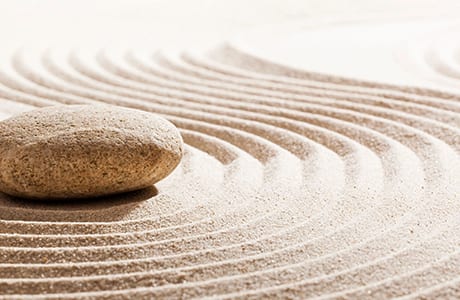 Smooth stone resting in raked sand of a zen garden